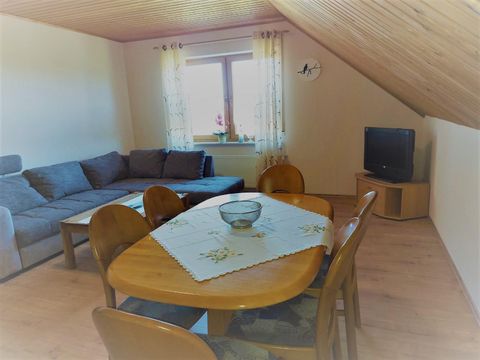 Een lichte woonkamer met een comfortabele bank en een eetgedeelte. Bij het raam staan gordijnen, en een televisie is ook aanwezig.