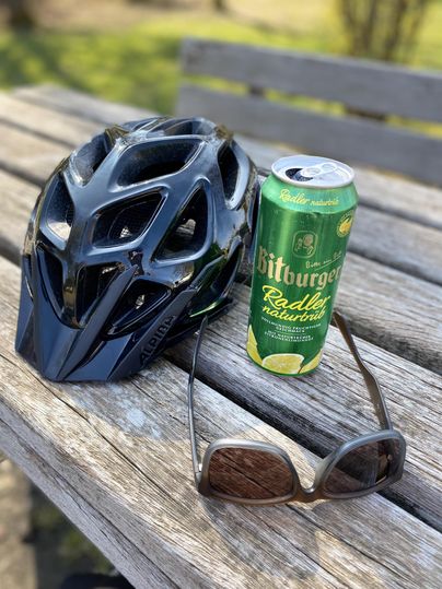 Un casque de vélo est posé à côté d'une canette de radler et d'une paire de lunettes de soleil sur une table. La scène transmet une sensation de détente après une balade à vélo.