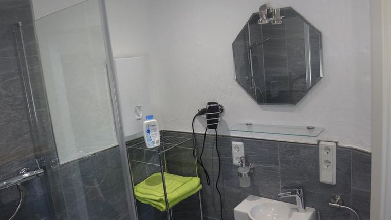 Une salle de bains moderne avec une douche en verre et des carrelages gris élégants. Un petit lavabo avec une serviette sur une étagère.