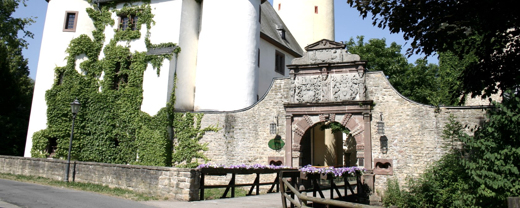Rittersdorf Castle with two round towers and a high yellow tower. An archway with decorations leads into the castle. Ivy grows on the walls., © Frank Schaal