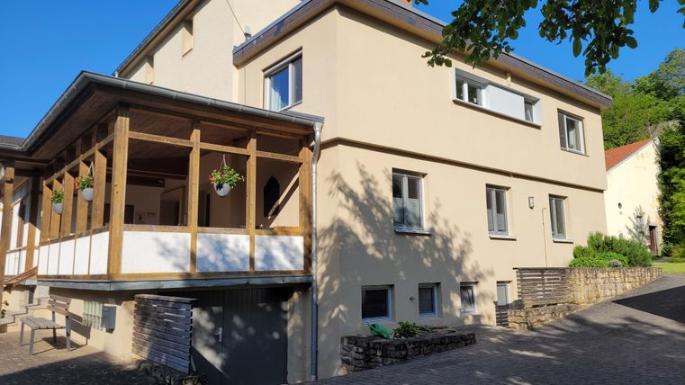 Ein modernes Haus mit einem überdachten Eingangsbereich und viel Tageslicht. Die Umgebung ist grün und einladend.