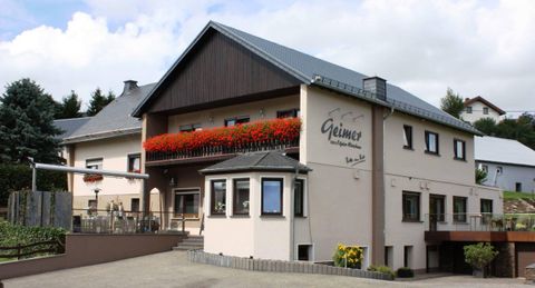 Un bâtiment charmant avec des balcons fleuris et un toit moderne. La façade est claire et accueillante, entourée d'un paysage verdoyant.