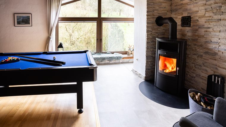 A cozy room with a pool table and a modern fireplace. Large windows provide a view of the green landscape outside.
