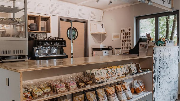 Ein modernes Café mit einem Empfangsbereich und einer Getränkebar. Die Theke ist gefüllt mit verschiedenen Snacks und Süßigkeiten.