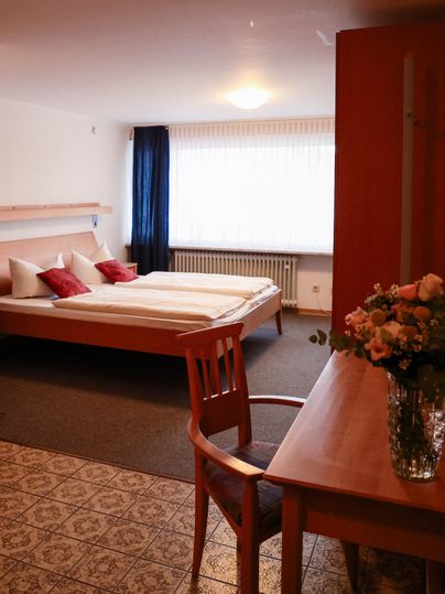 Une chambre confortable avec un grand lit et des coussins rouges. Une table avec un vase plein de fleurs est placée à côté du lit.