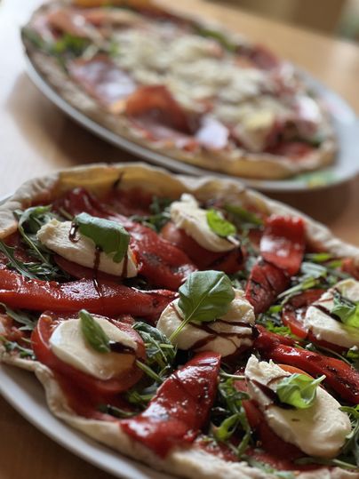 Zwei köstliche Pizzen auf Tellern. Die vordere Pizza ist mit rotem Paprika, Mozzarella und frischem Basilikum belegt.