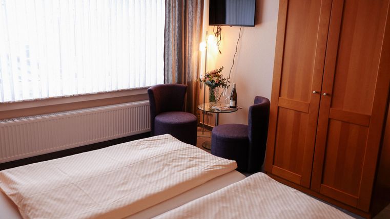 Une chambre confortable avec deux lits, une télévision à écran plat et un petit coin salon. Les grandes fenêtres laissent entrer beaucoup de lumière naturelle.