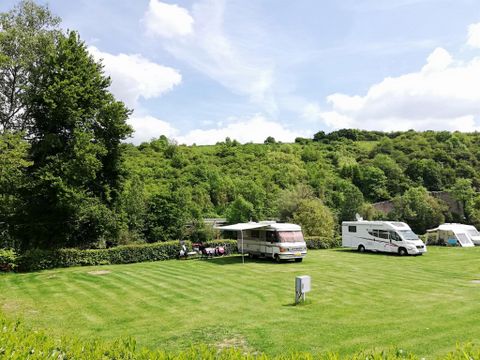 Een mooie camping met verschillende campers op een groene weide. Op de achtergrond zijn beboste heuvels en een heldere lucht te zien.