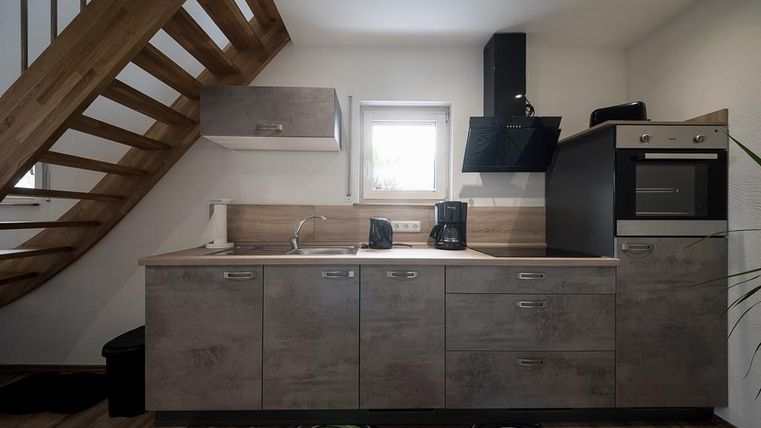 Une cuisine moderne avec des armoires en bois et un escalier confortable. L'équipement comprend un évier, une cuisinière et des machines à café.