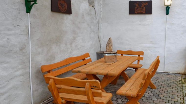 Un plateau en bois avec des bancs assortis se trouve dans une cour pavée. Des panneaux décoratifs et des lampes en forme de lanternes sont accrochés aux murs.