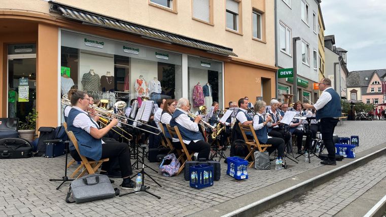 Eine Musikgruppe spielt auf der Straße. Die Musiker sitzen auf Stühlen und sind in passenden Outfits gekleidet.