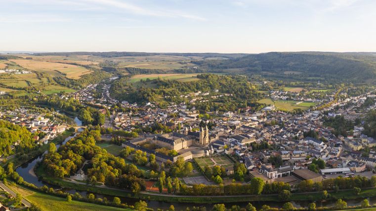 Eine malerische Aussicht auf ein kleines Dorf in einem grünen Tal. Die Umgebung ist hügelig und von Bäumen umgeben, während ein Fluss durch die Landschaft fließt.
