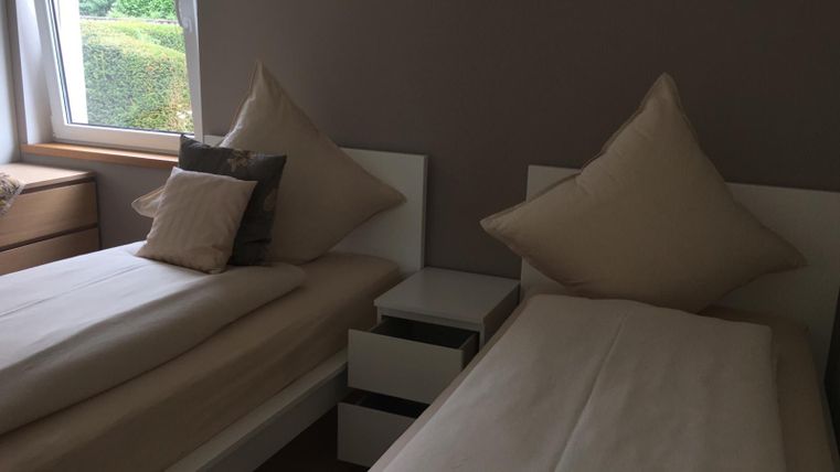 Een gezellige slaapkamer met twee eenpersoonsbedden en grote kussens. De kamer heeft een raam dat daglicht binnenlaat.