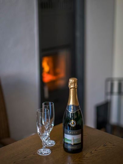 Eine Flasche Champagner steht auf einem Tisch neben zwei Gläsern. Im Hintergrund brennt ein Kamin und sorgt für eine gemütliche Atmosphäre.
