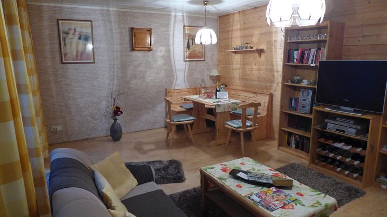 Ein gemütliches Wohnzimmer mit Holzpanelen und einer Essgruppe. Es gibt ein Sofa, einen Fernseher und eine warmen Atmosphäre.