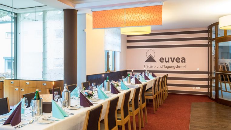 An elegant, bright dining hall with a set table and chairs. The tables are prepared with high-quality table linen and decorations for an event.