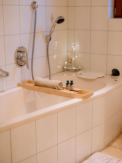 Ein modernes Badezimmer mit einer Badewanne und Holzelementen. Auf dem Wannenbrett befinden sich ein Handtuch und einige ätherische Öle.