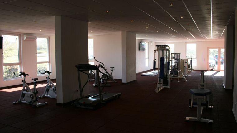 Een moderne sportschool met verschillende trainingsapparaten. Veel ruimte en grote ramen zorgen voor een heldere, uitnodigende sfeer.