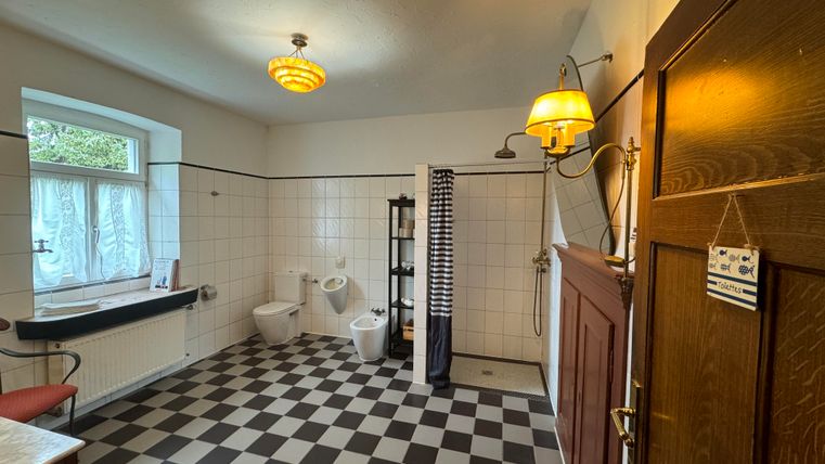 Une salle de bains moderne avec des carreaux noir et blanc et des fenêtres qui laissent entrer beaucoup de lumière naturelle. Il y a une douche, deux toilettes et un élégant meuble en bois.