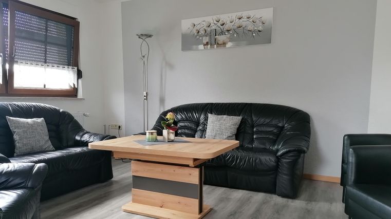 Ein gemütliches Wohnzimmer mit schwarzen Ledermöbeln und einem Holzkaffee Tisch. An der Wand hängt ein dekoratives Bild, und ein Stehlampe sorgt für zusätzliche Beleuchtung.