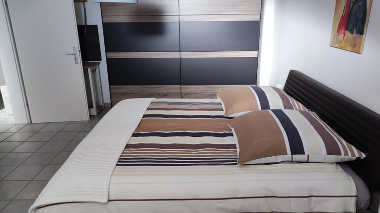 Ein gemütliches Schlafzimmer mit einem großen Bett und gestreiften Bettwäsche. Der Raum ist schlicht und modern eingerichtet mit einem Kleiderschrank und einem Tisch.