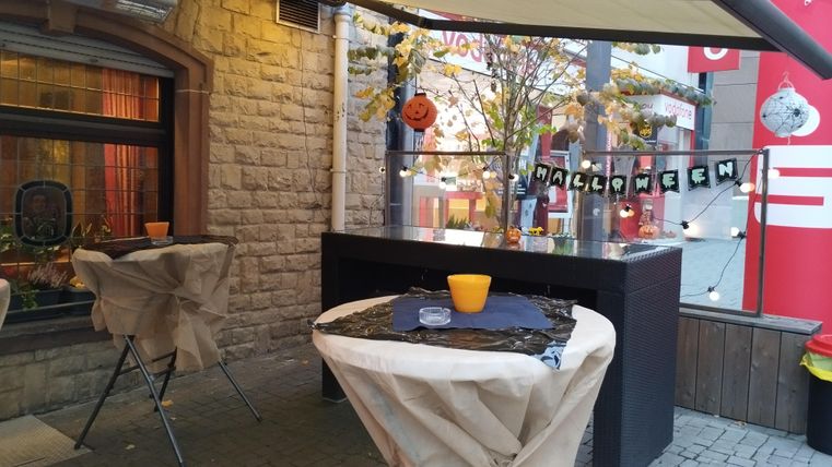 Ein dekorierter Außenbereich mit Tischen, die für Halloween vorbereitet sind. Die Atmosphäre ist festlich mit Kürbissen und einer Halloween-Dekoration.