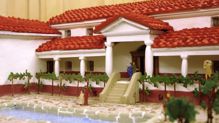 Ein Modell eines römischen Hauses mit roten Ziegeldächern und Säulen. Im Vordergrund sind ein Garten und ein Wasserbecken zu sehen.