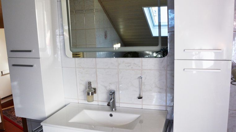 A modern bathroom with a white sink and a large mirror. The walls are tiled and there are white cabinets for storage.