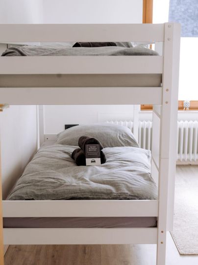Ein Etagenbett in einem hellen, modernen Zimmer. Auf der Bettdecke liegt ein Kissen und ein Handtuch.