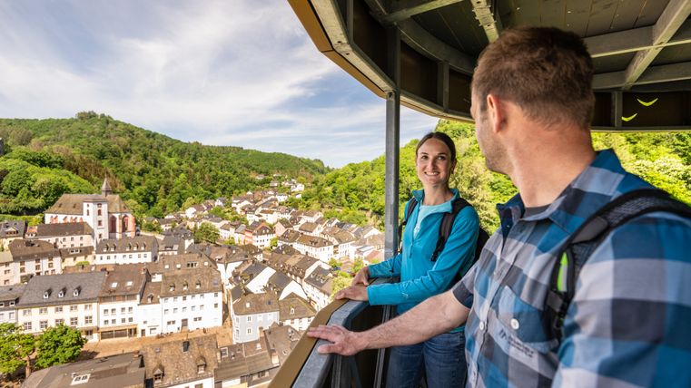 Zwei Personen auf einem Aussichtspunkt mit Blick auf eine Stadt und grüne Hügel.