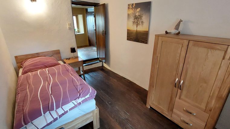 Een eenvoudige slaapkamer met een eenpersoonsbed en een houten kast. De kamer heeft een warme, uitnodigende uitstraling en een raam voor natuurlijke verlichting.