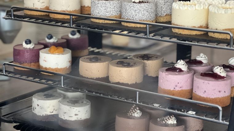 A selection of delicious cheesecakes in various colors and flavors. They are beautifully displayed on a shelf.