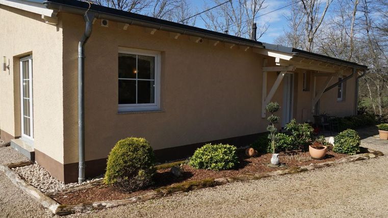 Une maison moderne de plain-pied avec un crépi clair et de grandes fenêtres. Le jardin est bien entretenu et décoré de plantes vertes et de pots.
