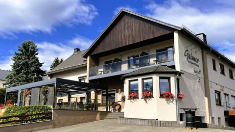 Ein charmantes Gebäude mit gelber Fassade und blühenden Balkonen. Darunter befindet sich eine Terrasse mit Sonnenschirm.