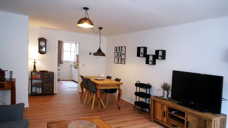 Een gezellige woonkamer met een eetgedeelte en een grote televisie. De lichte muren en de houten vloer zorgen voor een uitnodigende sfeer.