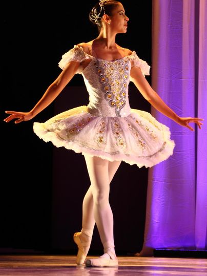 Eine Balletttänzerin in einem eleganten Kostüm steht in Pose auf der Bühne. Ihr Kleid ist verziert und sie strahlt Anmut und Schönheit aus.