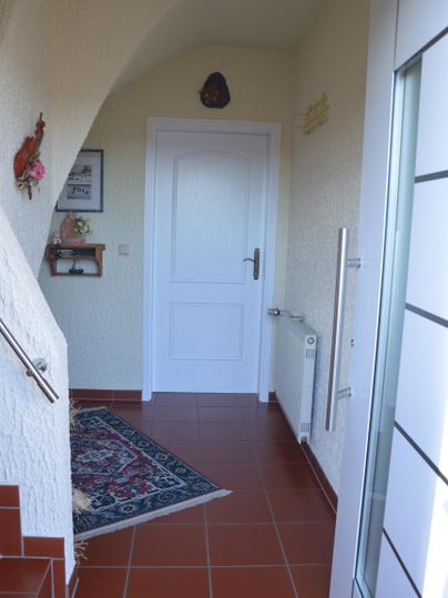 A bright entrance area with a carpet and a white door. The walls are done in neutral colors, and a staircase leads upstairs.