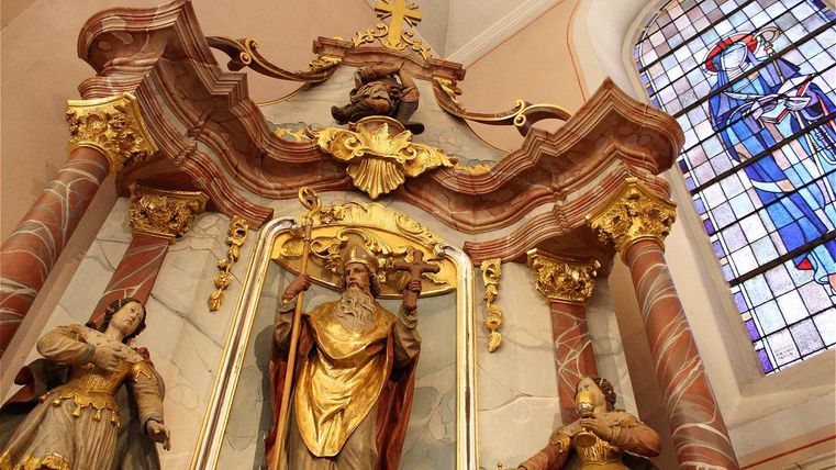 Un magnifique autel avec des ornements dorés et des statues de saints. En arrière-plan, on peut voir une fenêtre en vitraux colorés.