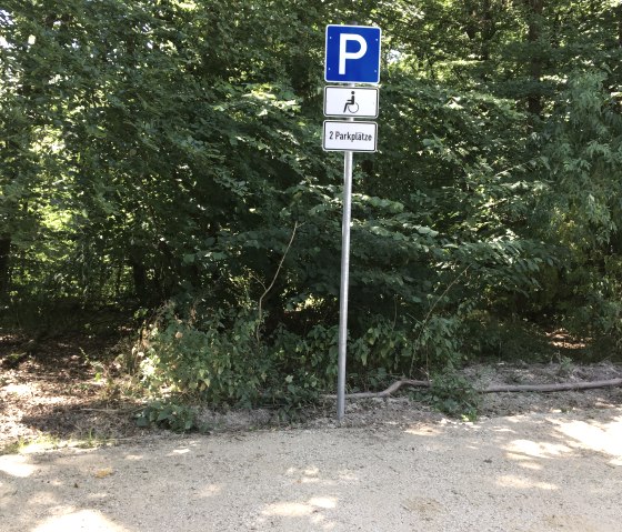 Ein Parkplatzschild f&uuml;r Behinderte im Wald. Es zeigt zwei verf&uuml;gbare Parkpl&auml;tze an. Umgeben von dichtem Gr&uuml;n und B&auml;umen., &copy; TI Bitburger Land