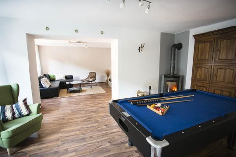 A game room with a pool table and a cozy living room in the background. The space has a modern and inviting style.