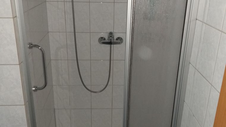 A modern shower cubicle with a glass door and sanitary installations. The walls are tiled with white tiles.