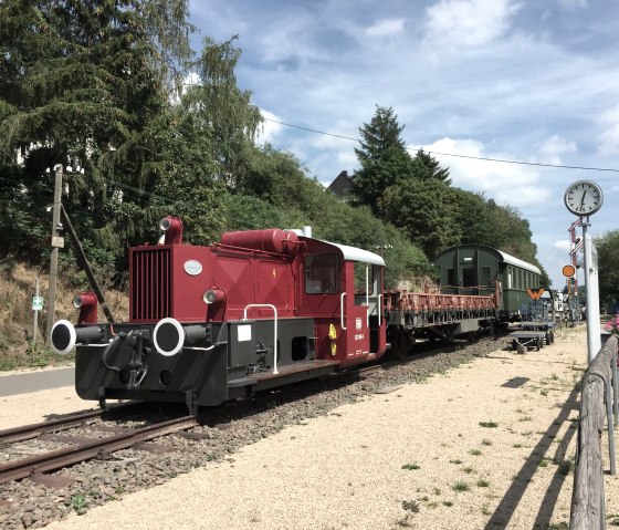 Rote Lokomotive und alte Waggons auf Gleisen am alten Bahnhof in Pronsfeld, umgeben von B&auml;umen und Blumen., &copy; Eifel Tourismus GmbH