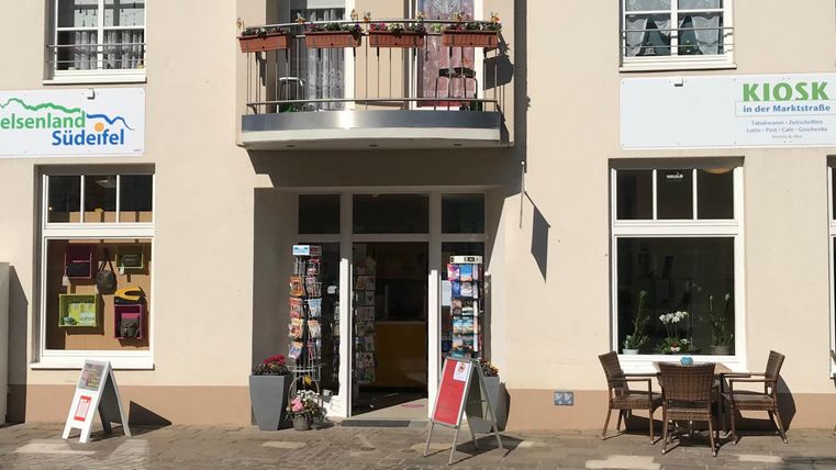 Een vriendelijke winkel met een kiosk en een informatiecentrum. Buiten staan tafels en stoelen voor gasten.