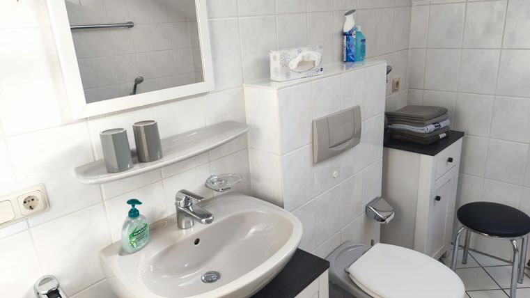 Ein modernes Badezimmer mit Waschbecken, Spiegel und Toilette. Der Raum ist hell und mit weißen Fliesen ausgestattet.