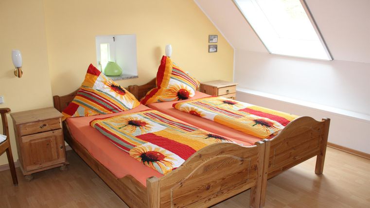 Een gezellige slaapkamer met twee bedden van hout en kleurrijke dekbedden. De muren zijn in een warme gele tint en er is een raam met natuurlijk licht.