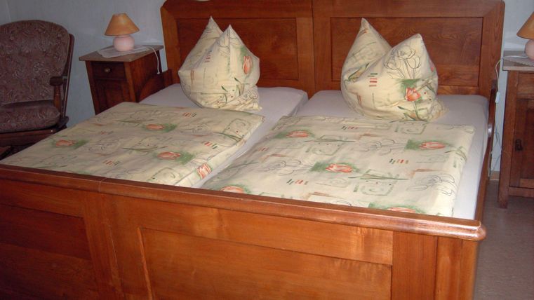 Une chambre confortable avec un lit en bois et deux oreillers. À côté du lit se trouve une table de nuit avec une lampe.