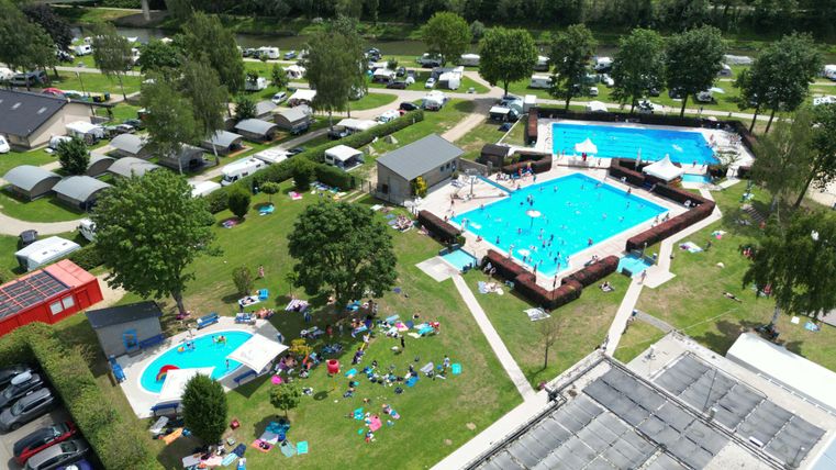 Un terrain de camping avec deux piscines et de nombreux espaces de repos. Les enfants et les adultes profitent du temps ensoleillé et des activités de loisirs.