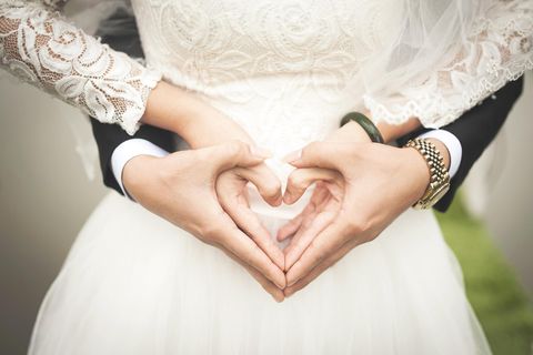 Zwei Hände formen ein Herz, während sie einen Brautkleid tragen. Es symbolisiert Liebe und Zuneigung.