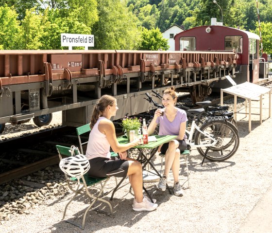 Zwei Frauen sitzen an einem Tisch im Freien vor einem alten Zug im Eisenbahnmuseum Pronsfeld. Fahrräder stehen daneben., © Eifel Tourismus GmbH, Dominik Ketz