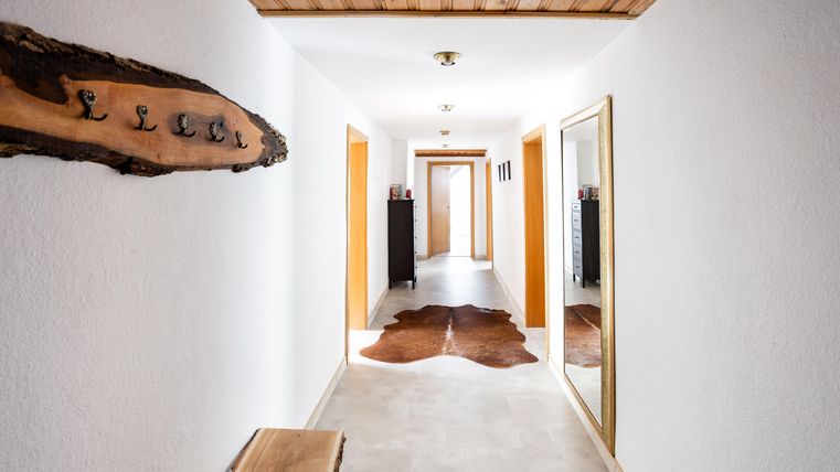 A bright hallway with white wall paint and wood details. Hooks are hanging on the wall, and a large mirror is also present.